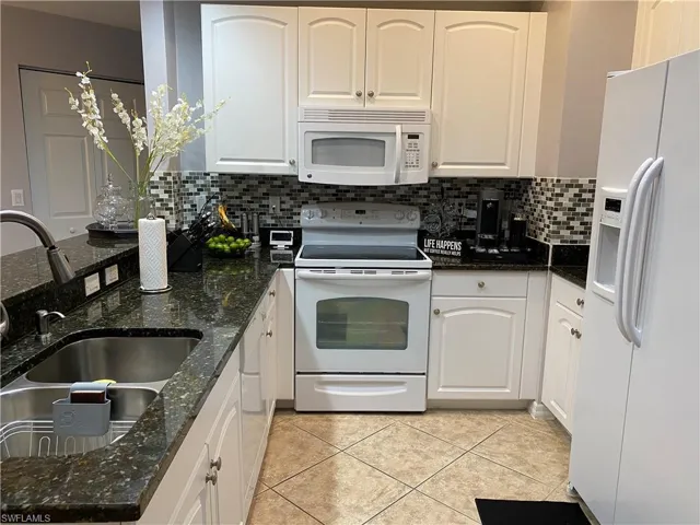 Kitchen with tasteful backsplash, white appliances, and dark stone counters