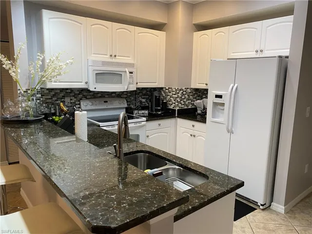 Kitchen with white cabinetry, dark stone counters, white appliances, and decorative backsplash