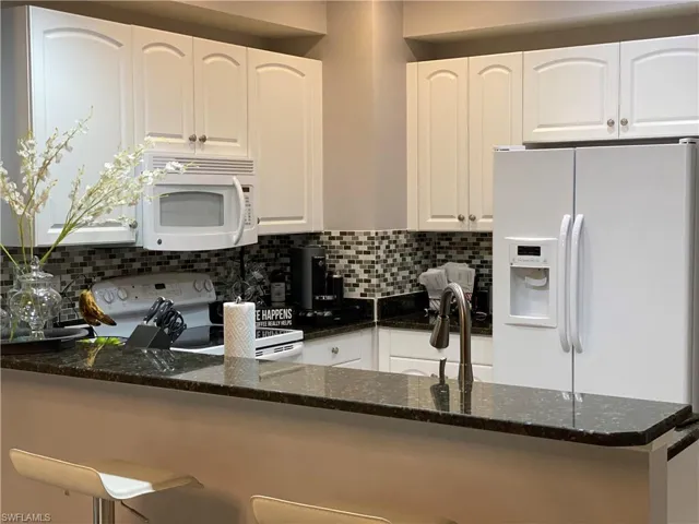 Kitchen featuring dark stone counters, white cabinets, and white appliances