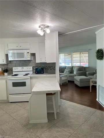 Kitchen featuring backsplash, white cabinets, light stone countertops, and stove