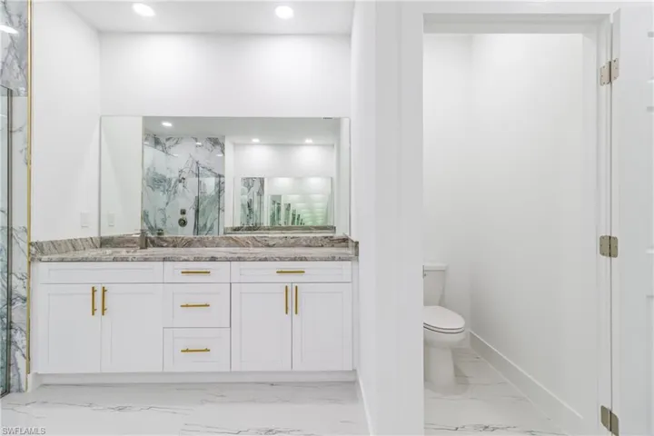 Bathroom with a marble finish shower, double vanity, light marble finish floors, and recessed lighting