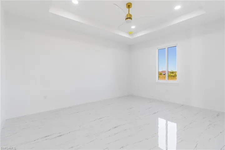 Unfurnished room with recessed lighting, ceiling fan, light marble finish flooring, and a tray ceiling
