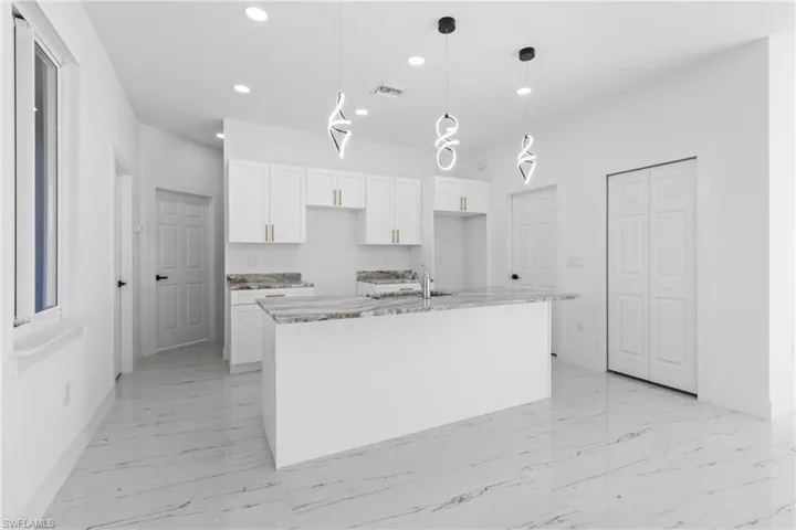 Kitchen featuring white cabinetry, light stone counters, pendant lighting, a kitchen island with sink, and light marble finish flooring