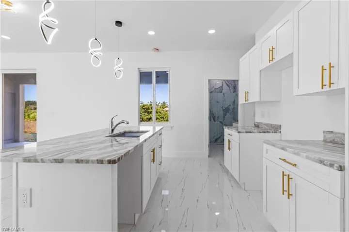 Kitchen featuring white cabinets, a center island with sink, pendant lighting, and light stone countertops