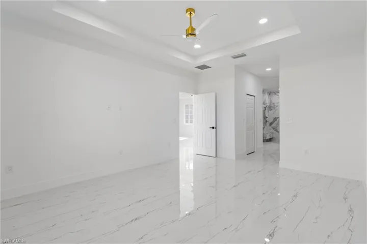 Spare room featuring a raised ceiling, recessed lighting, a ceiling fan, and light marble finish floors