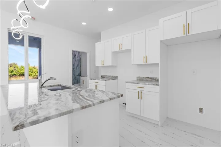 Kitchen with white cabinetry, light stone counters, an island with sink, and pendant lighting