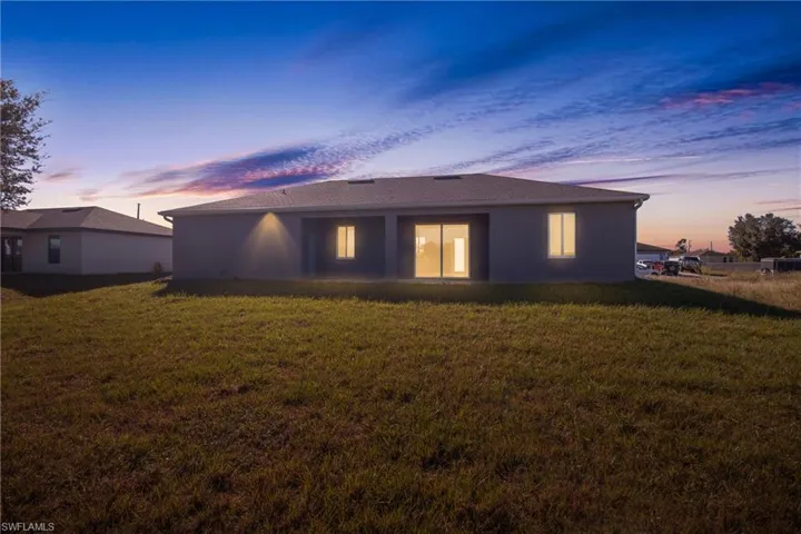 Back of property at dusk with a lawn, a patio area, and stucco siding