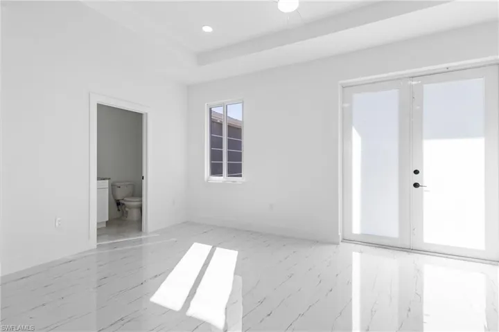 Unfurnished bedroom with connected bathroom, light marble finish flooring, recessed lighting, and a tray ceiling