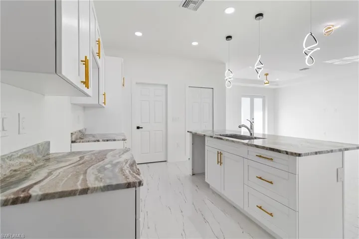 Kitchen with white cabinetry, light stone countertops, hanging light fixtures, and a kitchen island with sink