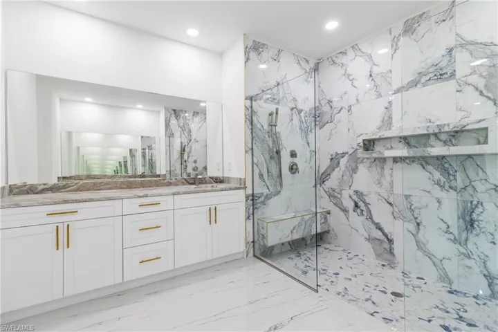 Bathroom featuring vanity, a marble finish shower, recessed lighting, stone wall, and light marble finish flooring