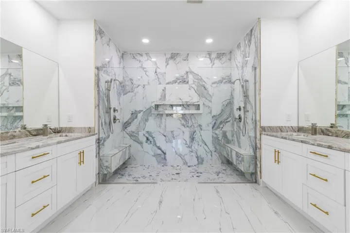 Bathroom with two vanities, a marble finish shower, and recessed lighting