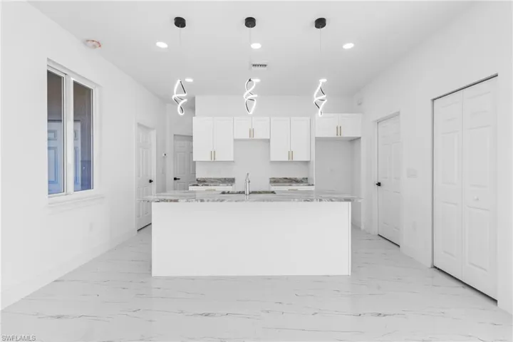 Kitchen featuring white cabinets, light stone countertops, pendant lighting, and a kitchen island with sink