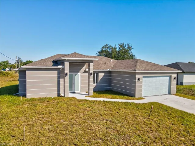 Single story home with a front lawn, french doors, an attached garage, a shingled roof, and concrete driveway