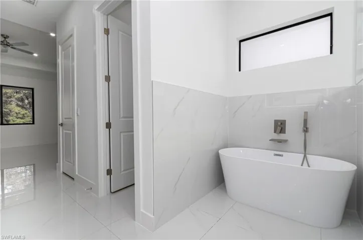 Full bath with a wainscoted wall, a freestanding bath, marble finish floor, and a healthy amount of sunlight