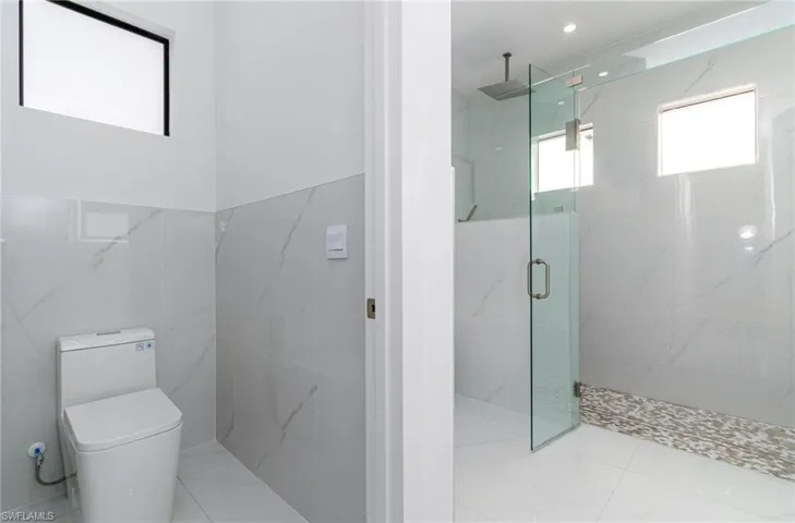 Full bath with a marble finish shower, tile walls, and toilet