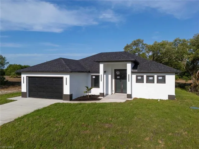 View of front facade featuring stucco siding, a shingled roof, a front yard, concrete driveway, and an attached garage