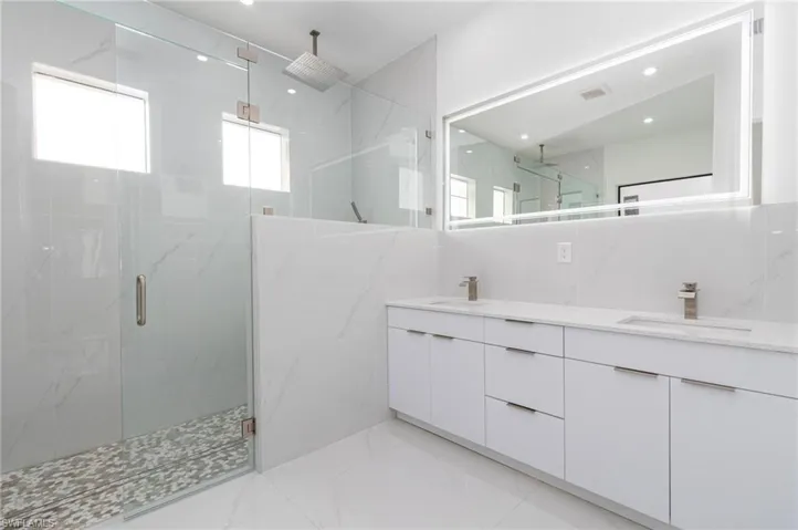 Bathroom with a marble finish shower, a sink, double vanity, and visible vents