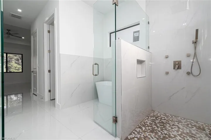 Full bathroom with tile walls, a freestanding tub, ceiling fan, visible vents, and a marble finish shower