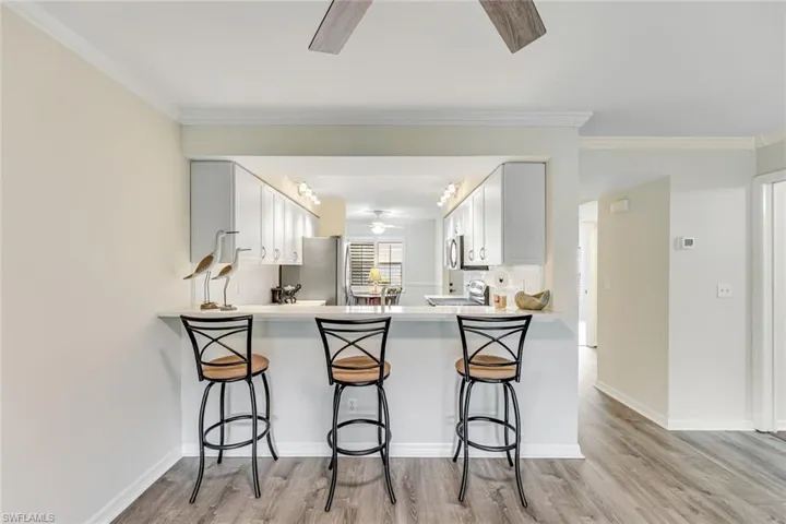 Kitchen pass-through with a breakfast bar, light cabinetry, stainless steel appliances, and wood-finish flooring