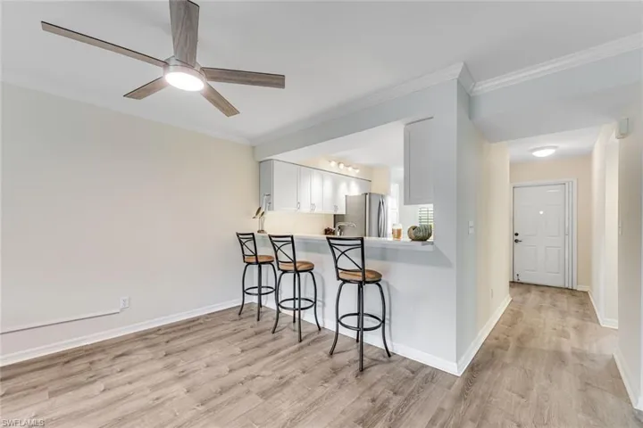 Open-concept living space featuring wood-finish flooring, a modern ceiling fan with integrated lighting, and crown molding