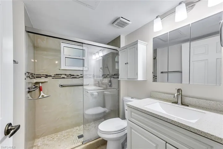 Bathroom featuring a glass-enclosed shower with tile surround and mosaic accent, a wall-mounted grab bar, and a window
