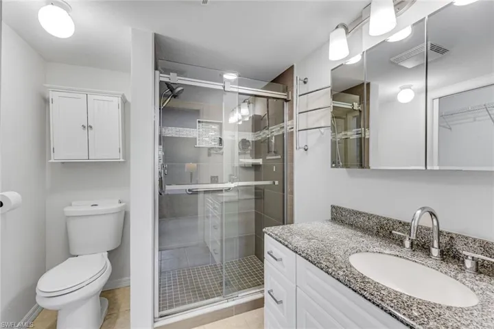 Contemporary bathroom featuring a spacious glass-enclosed shower with tile surround, a white vanity with granite-finish countertop and undermount sink, and a multi-door mirrored medicine cabinet