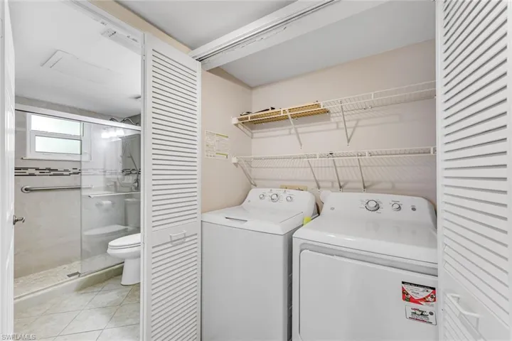 Dedicated laundry area featuring a white top-load washer and dryer, louvered bi-fold doors, and wire shelving for organization