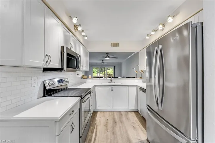 Bright kitchen featuring white cabinetry, stainless steel appliances, a subway tile backsplash, white countertops, and wood-finish flooring