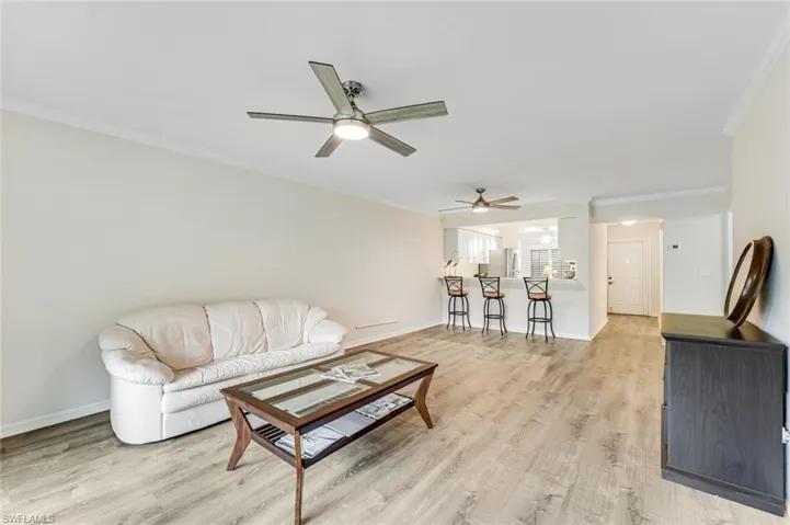 Open-concept living area with wood-finish flooring, two ceiling fans, and a breakfast bar