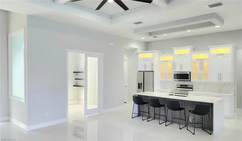 Kitchen with a breakfast bar, white cabinetry, stainless steel appliances, a center island with sink, and glass fronted cabinets
