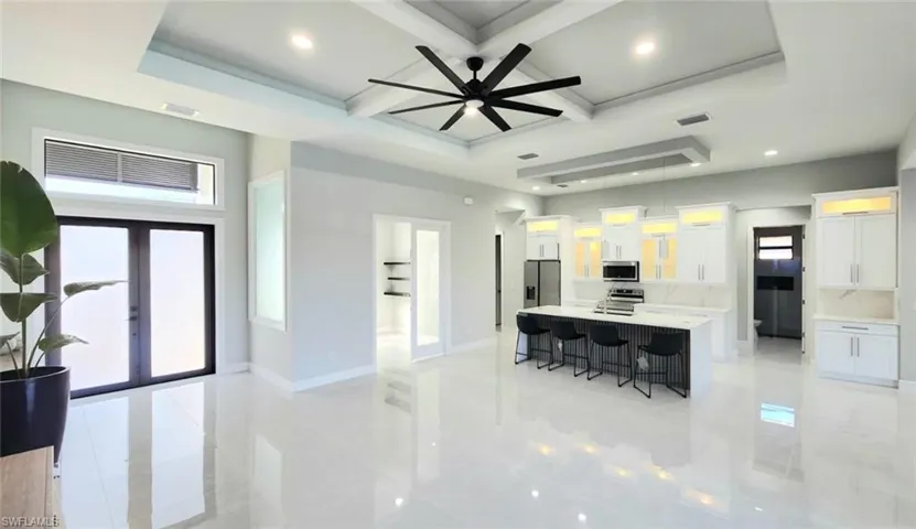 Dual tone kitchen with a breakfast bar, a spacious island, coffered ceiling, light stone countertops, and recessed lighting