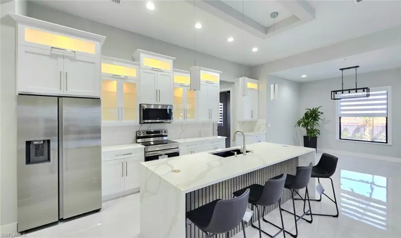 Kitchen with stainless steel appliances, light stone counters, tasteful backsplash, white cabinets, and a center island with sink