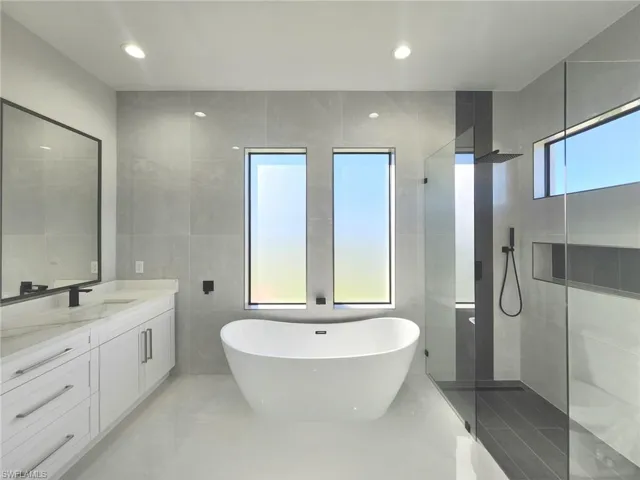 Bathroom featuring walk in shower, vanity, a freestanding tub, tile walls, and recessed lighting