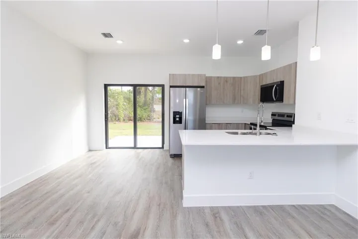 Kitchen with hanging light fixtures, light stone counters, stainless steel appliances, a peninsula, and modern cabinets