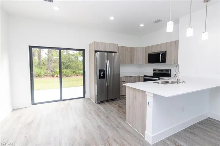 Kitchen with stainless steel appliances, a peninsula, pendant lighting, light wood-type flooring, and recessed lighting