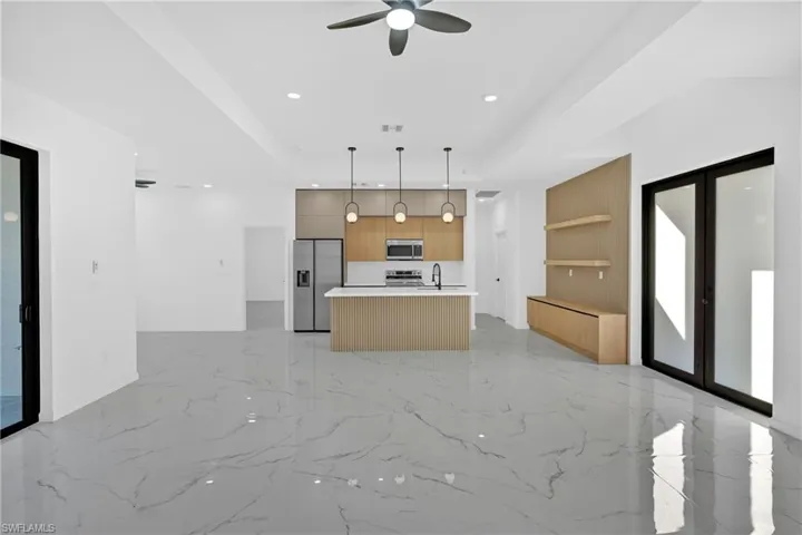 Kitchen with open floor plan, decorative light fixtures, stainless steel appliances, light countertops, and an island with sink