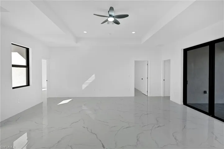 Unfurnished room featuring a tray ceiling, a ceiling fan, recessed lighting, and light marble finish flooring
