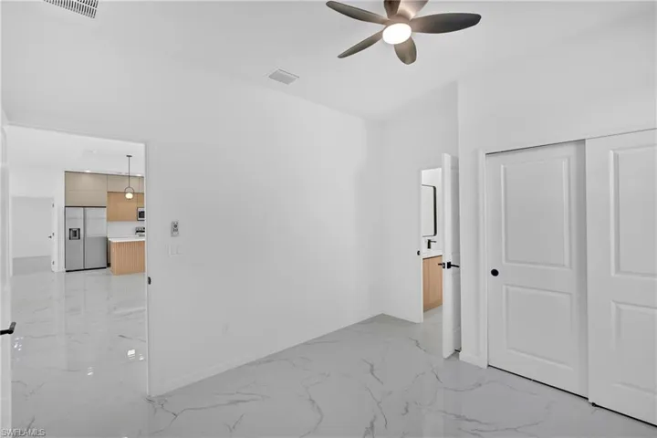 Unfurnished bedroom featuring light marble finish floors, stainless steel built in refrigerator, a closet, and a ceiling fan