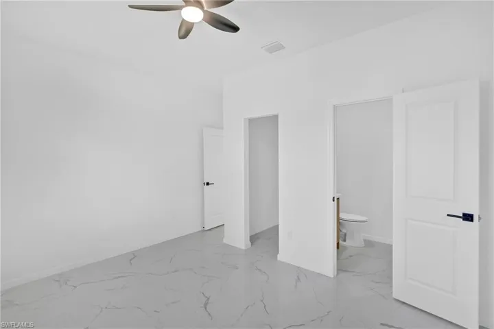 Unfurnished bedroom with light marble finish flooring, ceiling fan, and connected bathroom