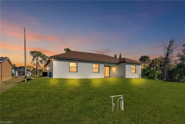 Back of property at dusk with stucco siding and a lawn