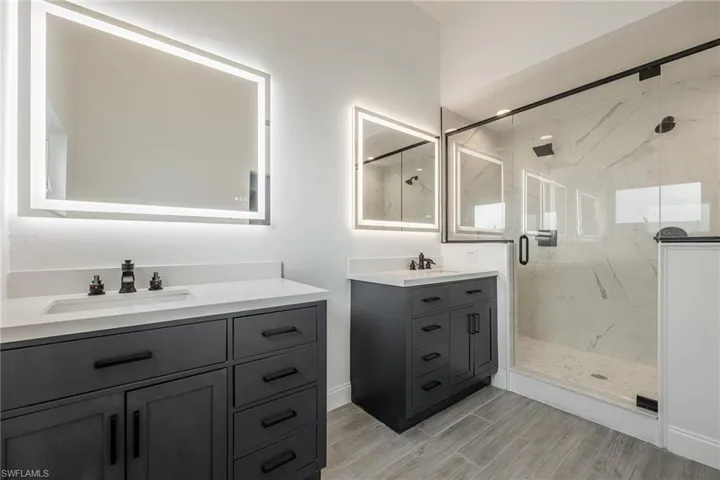Bathroom with wood finished floors, two vanities, a sink, and a marble finish shower