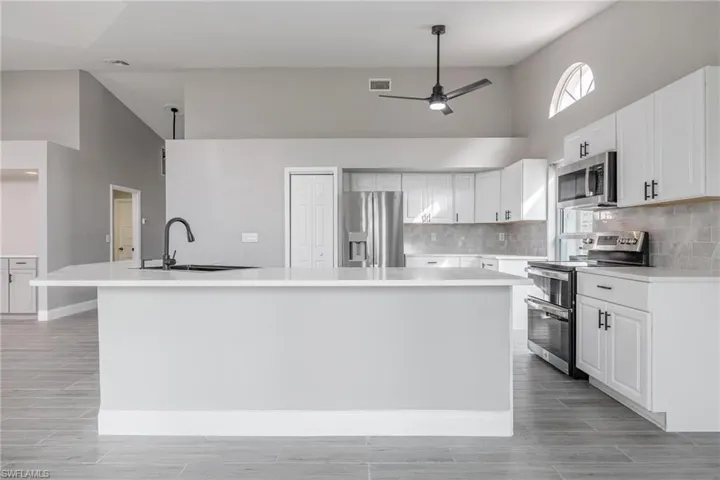 Kitchen featuring light countertops, a spacious island, a ceiling fan, a high ceiling, and stainless steel appliances