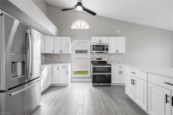 Kitchen with vaulted ceiling, light countertops, stainless steel appliances, white cabinets, and ceiling fan