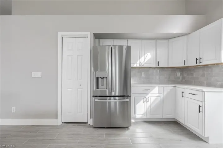 Kitchen featuring decorative backsplash, light countertops, white cabinets, baseboards, and stainless steel fridge with ice dispenser