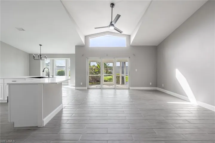 Unfurnished living room featuring vaulted ceiling, ceiling fan with notable chandelier, baseboards, a sink, and wood finished floors