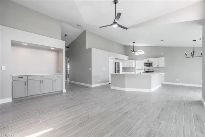Unfurnished living room featuring ceiling fan with notable chandelier, light wood-style floors, baseboards, and a sink