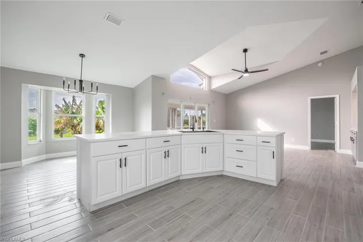 Kitchen with wood tiled floor, vaulted ceiling, white cabinets, and a sink