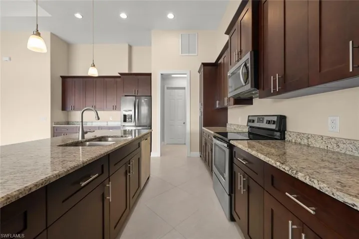 Kitchen featuring sink, light stone counters, decorative light fixtures, dark brown cabinets, and appliances with stainless steel finishes