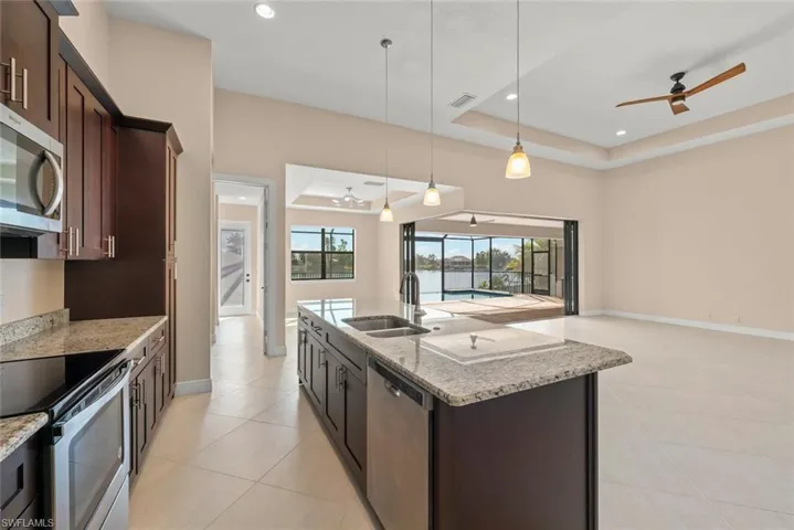 Kitchen featuring sink, hanging light fixtures, stainless steel appliances, a center island with sink, and a raised ceiling