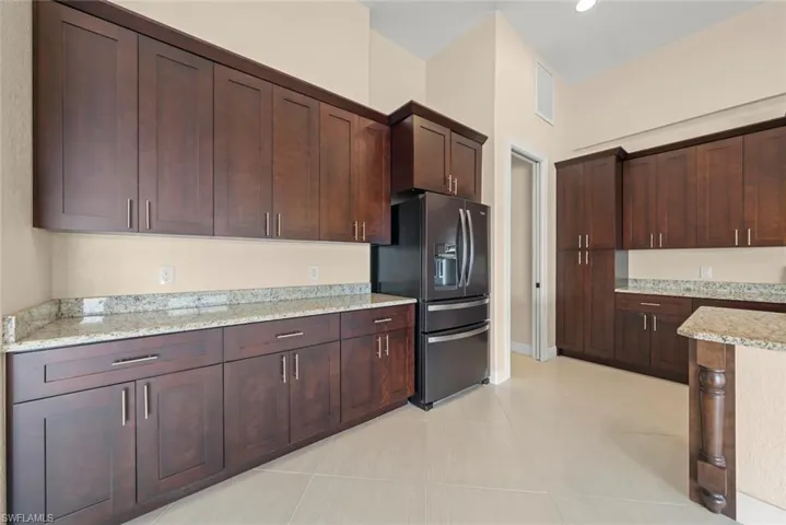 Kitchen featuring light stone countertops, light tile patterned floors, dark brown cabinetry, and stainless steel fridge with ice dispenser